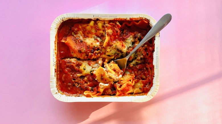 lasagna in paper tray with spoon on pink