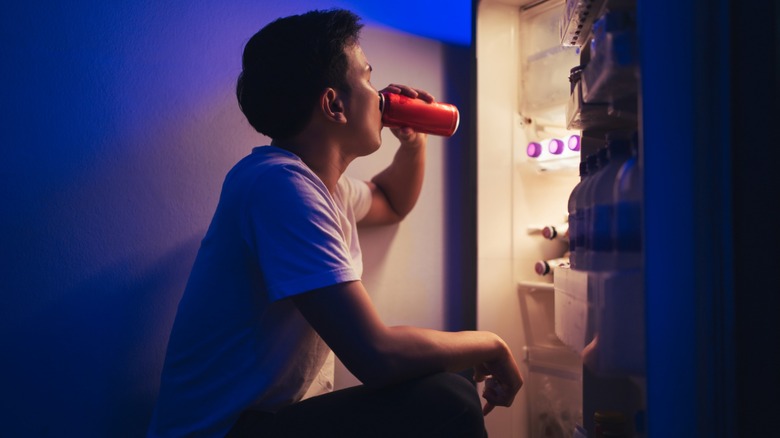 Man drinking soda in front of open fridge
