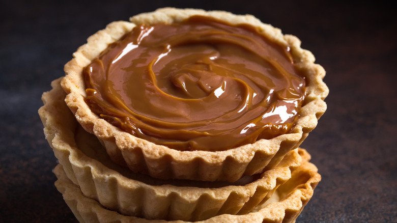 Stack of three small caramel tarts on black background