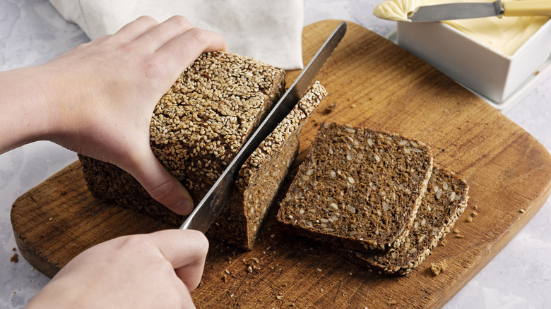 Hands slicing rye bread on wooden board