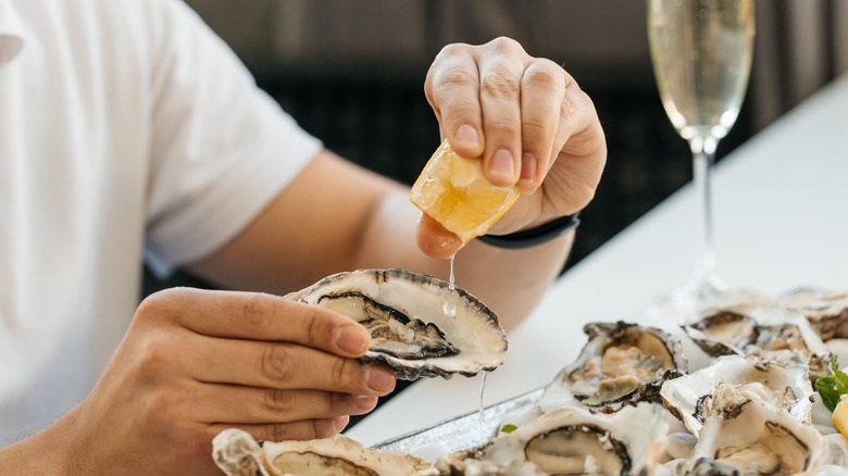 man squeezing lemon over raw oysters at table