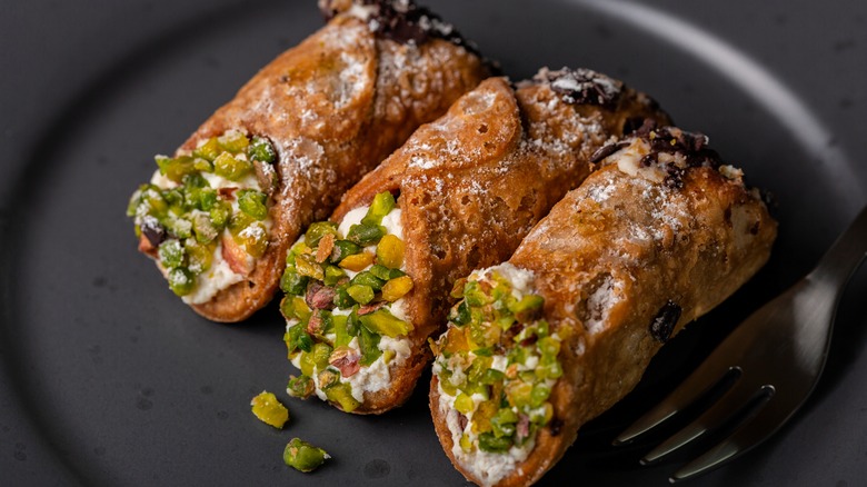 three cannoli on plate with crushed pistachios