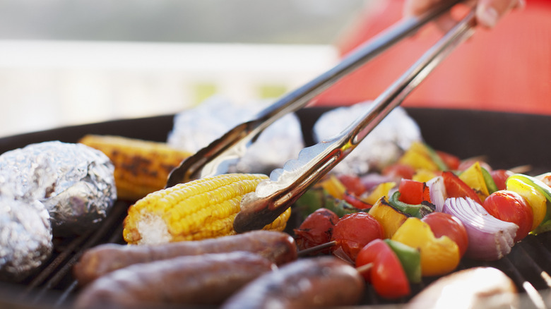 grilling corn with tongs, veggies, and sausage