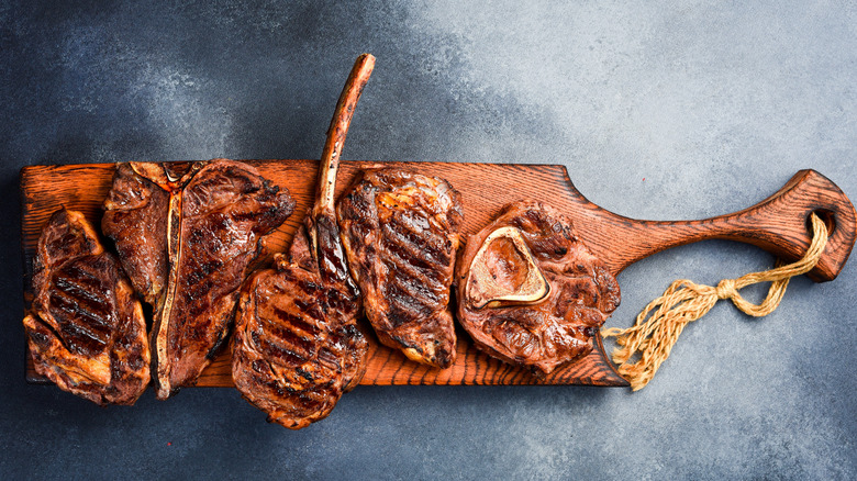 A medium rare steak on a chopping board with cherry tomatoes and fresh rosemary.