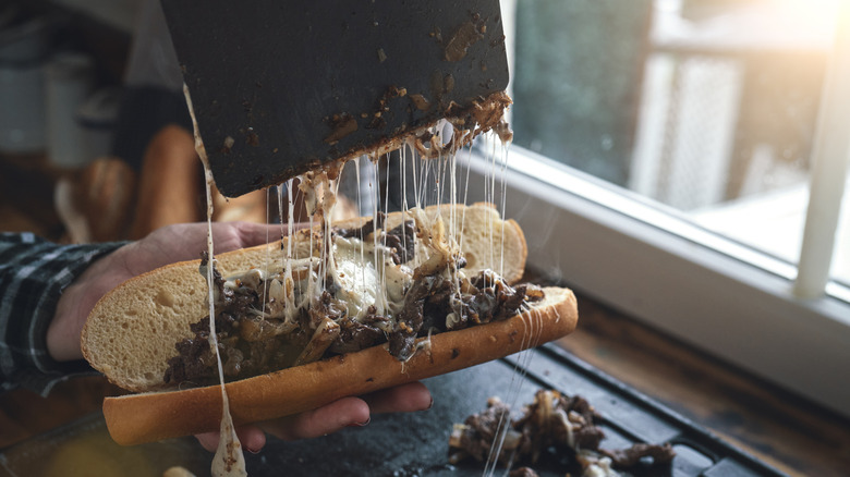 A Philly cheesesteak with the cheese melting as it is pulled away by a wide knife