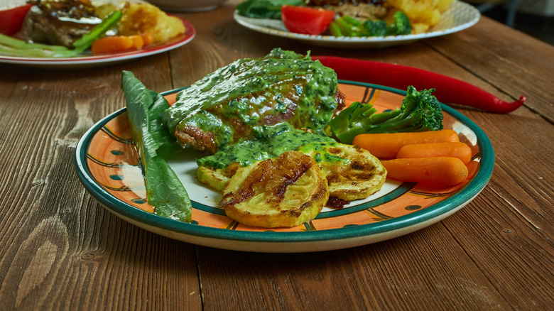 Stead de burgo with a green sauce and vegetables on the side