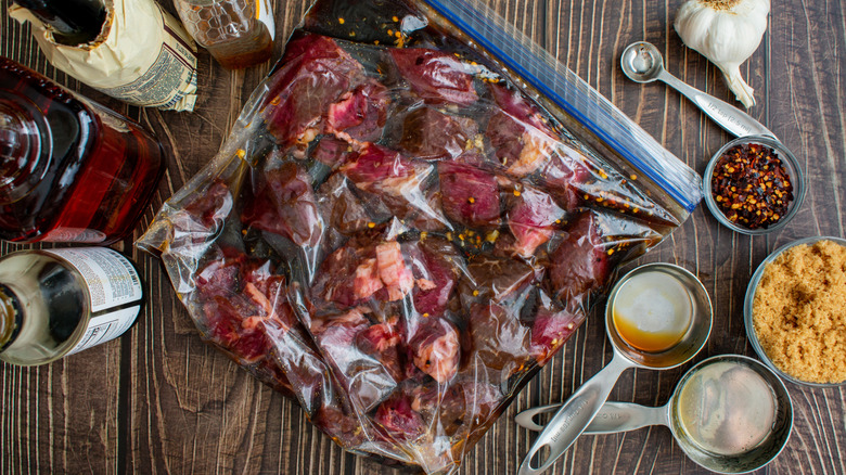 Raw steak tips marinating in a plastic bag surrounded by marinade ingredients