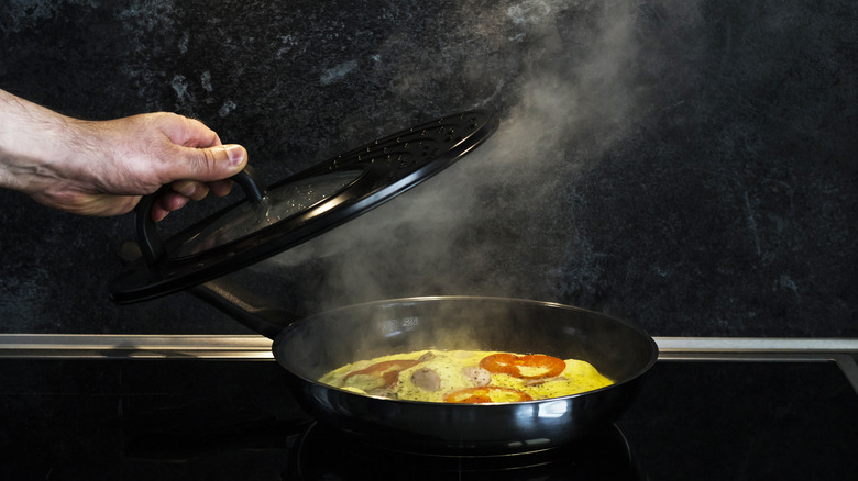 Frying pan on stove with cook holding cover