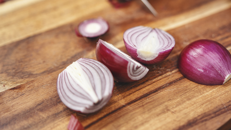 Red onions halved lengthwise on wooden board