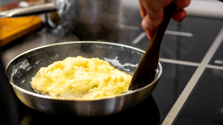 Hand stirring scrambled eggs in pan with spatula