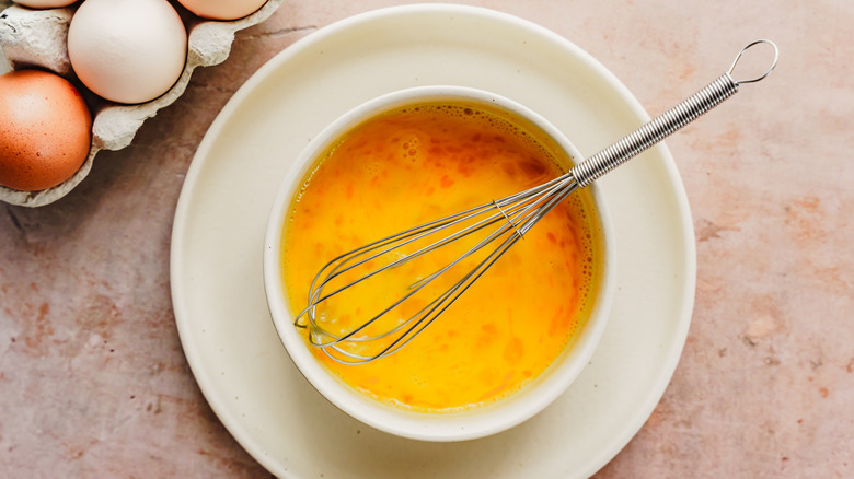 Raw scrambled eggs in bowl with whisk