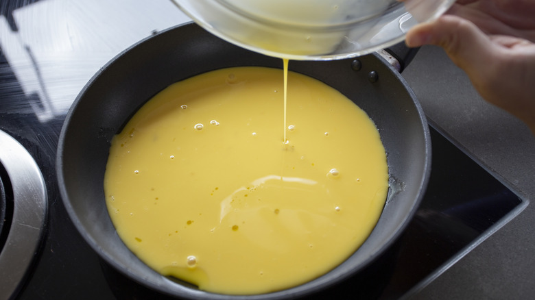 Pouring raw scrambled eggs into pan