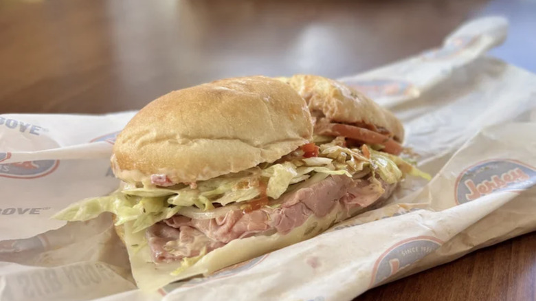 Jersey's Mikes sub sandwich with lettuce, tomato, meat, and other toppings on top of a paper wrapping and a paper bag