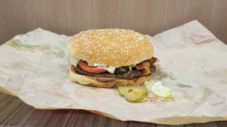 Burger King BLT on top of paper wrapping with a pickle and a piece of lettuce laying in front of the burger