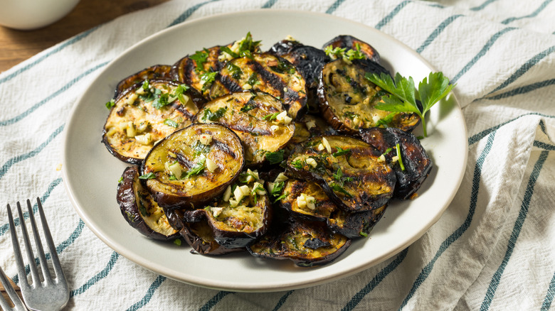 grilled eggplants layered on white plate with parsley, garlic