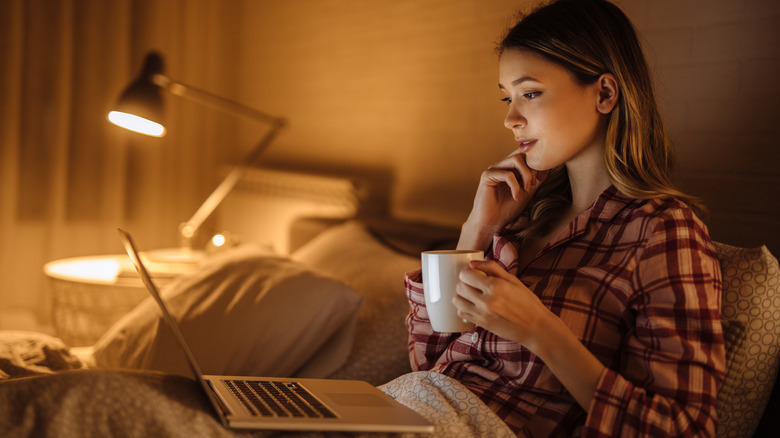 Woman with coffee and laptop in bed