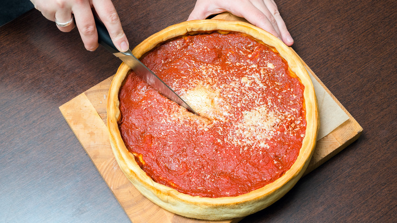 hands cutting deep dish pizza