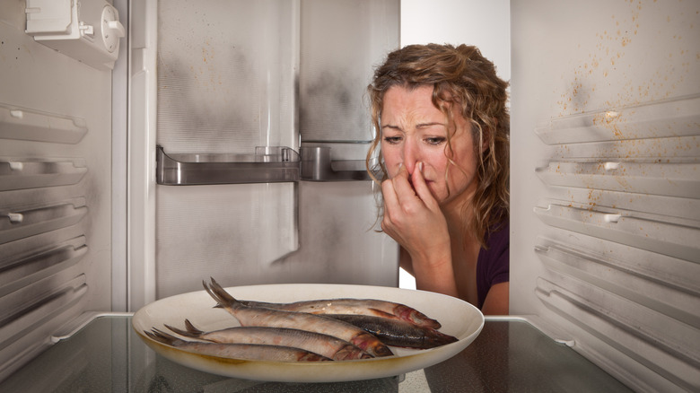 Woman pinching her nose while looking at a plate of spoiled fish