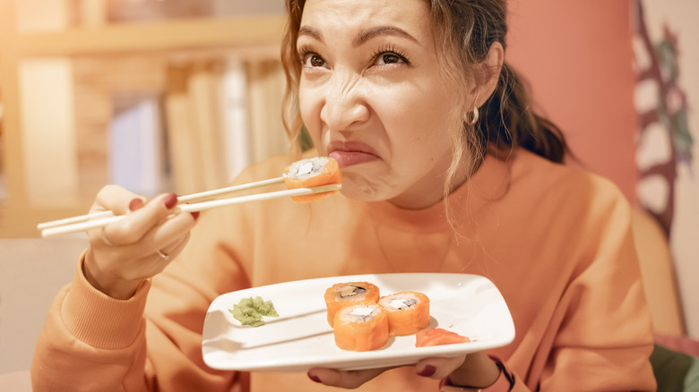 Woman sniffing bad smell from spoiled sushi roll