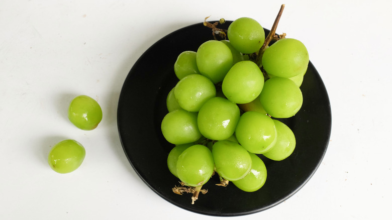 Black plate with bunch of green grapes