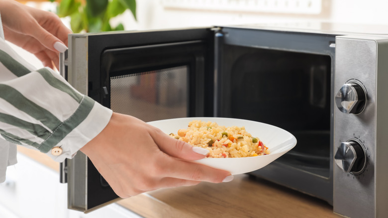 Woman's hand putting bowl of rice with veggies into microwave