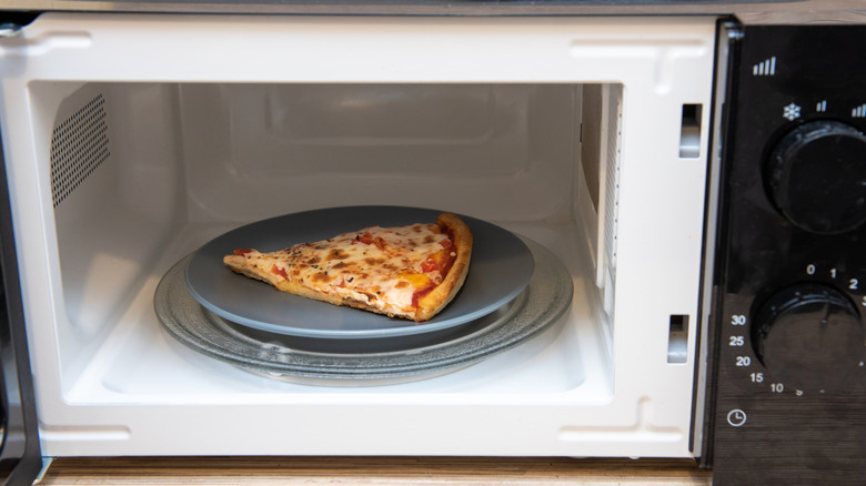 Slice of pizza on plate inside opened microwave