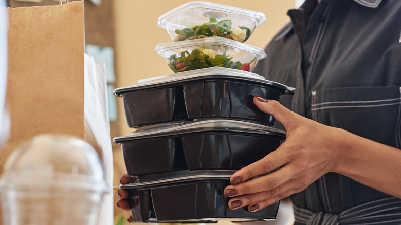 Woman's hands holding stack of plastic to-go boxes