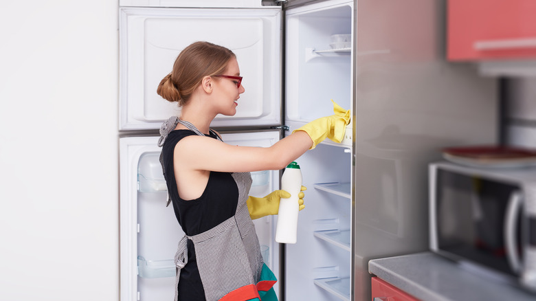 woman cleaning fridge with yellow gloves and apron