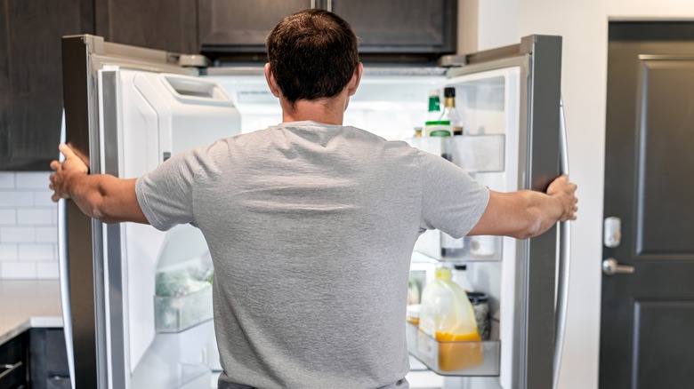 man standing at open refrigerator 