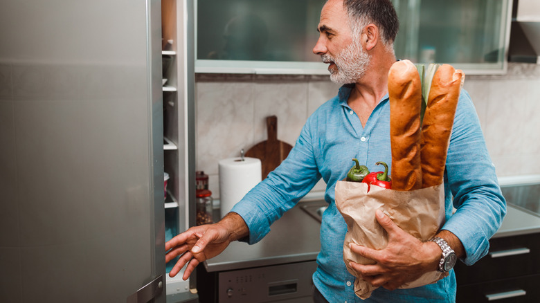 man with bread opening fridge