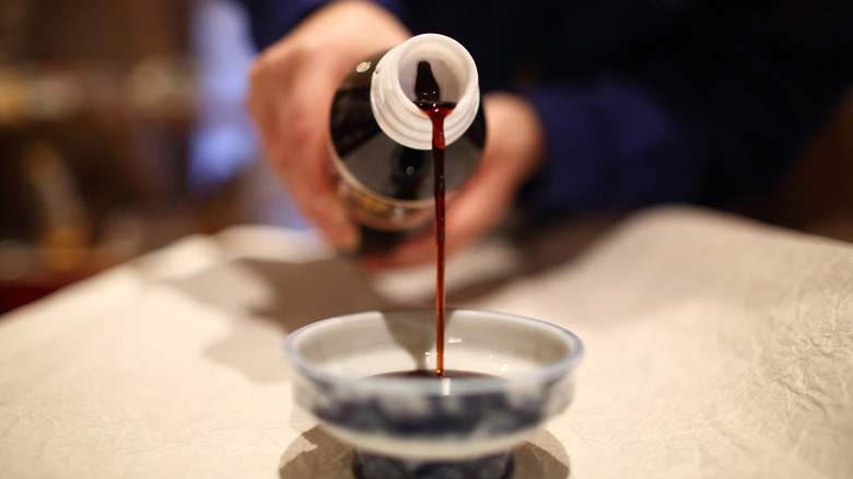 someone pouring soy sauce in a bowl