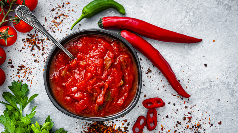 Bowl of diced tomatoes surrounding by chili peppers and cilantro