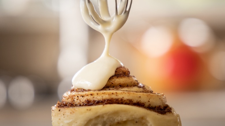 a whisk drips frosting onto a cinnamon roll