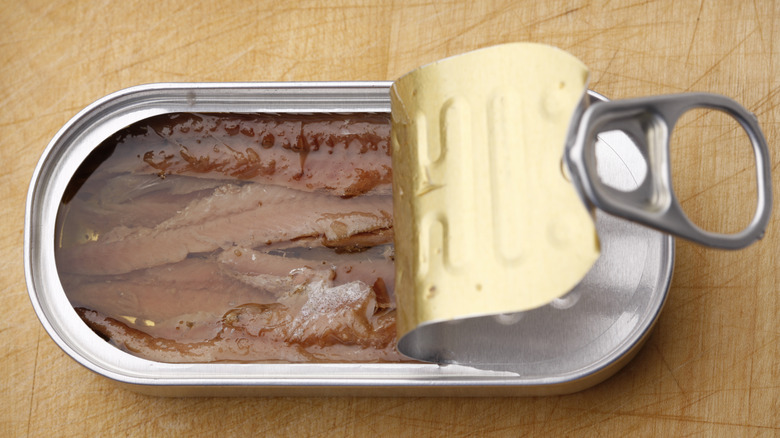 Half-opened can of anchovies on wooden cutting board