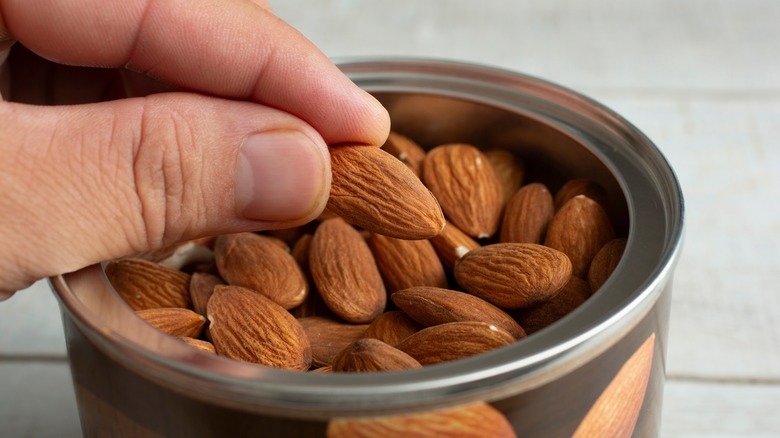 Fingers grabbing an almond from an opened tin