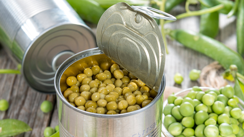 Opened can of peas with fresh ones surrounding it