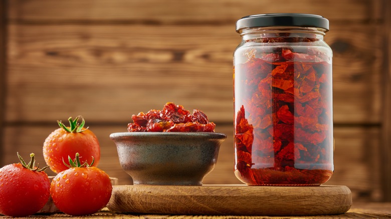 Bowl and jar of sun-dried tomatoes with fresh ones alongside