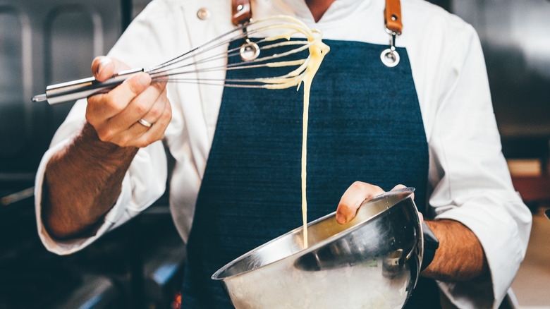 Chef whisking mayonnaise in metal bowl