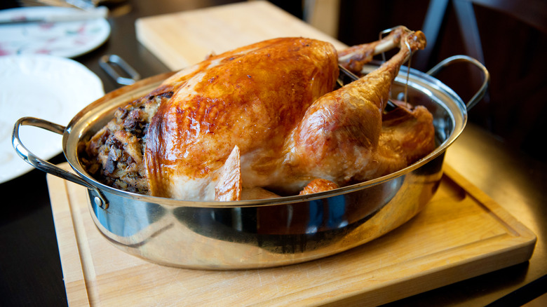 Roasted turkey resting in metal cooking pan on wood board