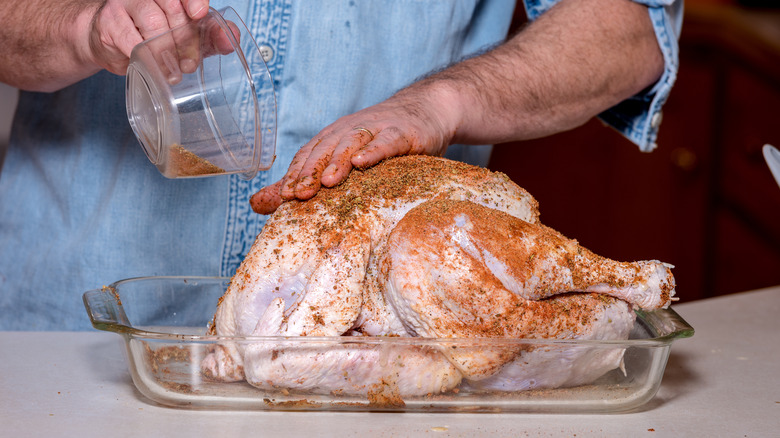 Man rubbing spices on skin of raw turkey