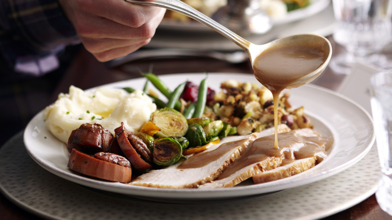 Man pouring gravy on dinner plate with turkey