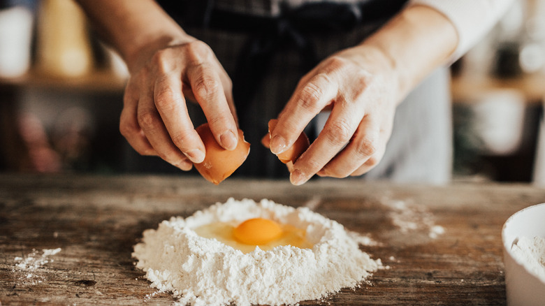person breaking egg into flour