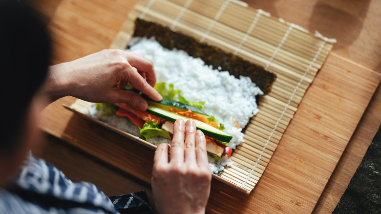 person rolling sushi on bamboo