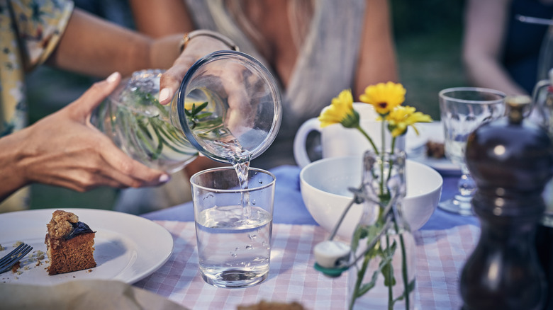 Hands using pitcher to pour water into glass at outdoor dining table