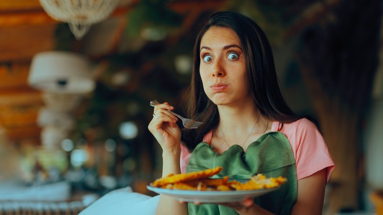 Woman with wide-eyed expression and a napkin tucked in her shirt holding plate of food