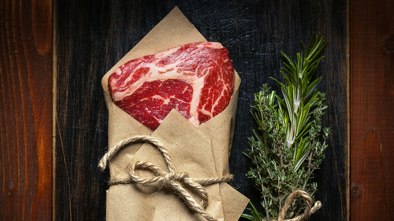 steak wrapped in butchers paper next to herb sprigs