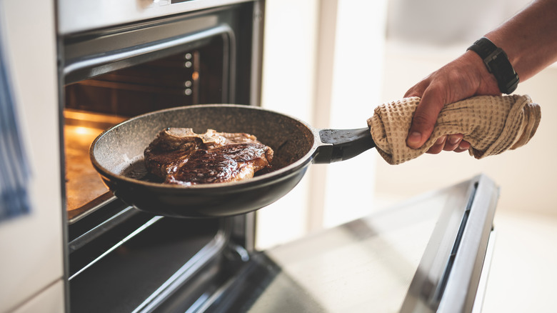 Hand placing pan of steak in oven