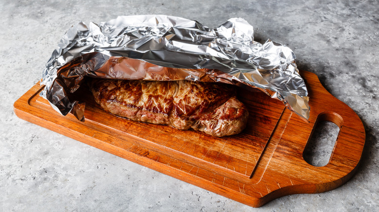 Foil on steak, sitting on wooden cutting board