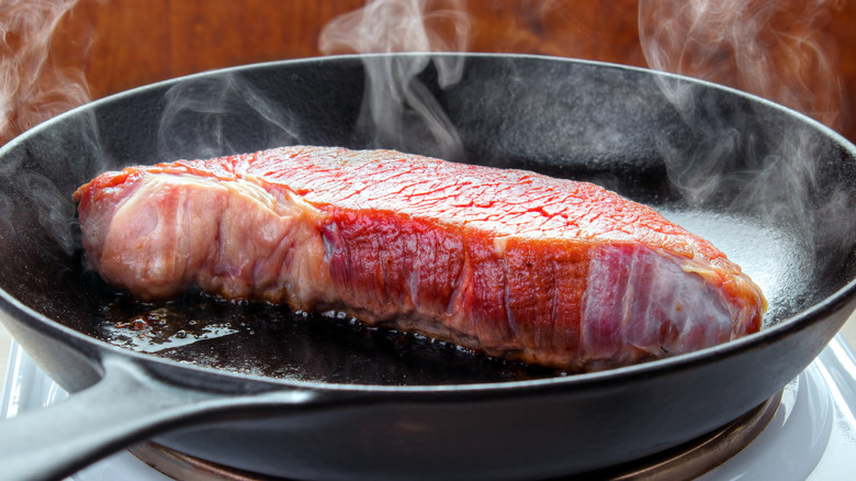 Raw steak sizzling smoking iron pan