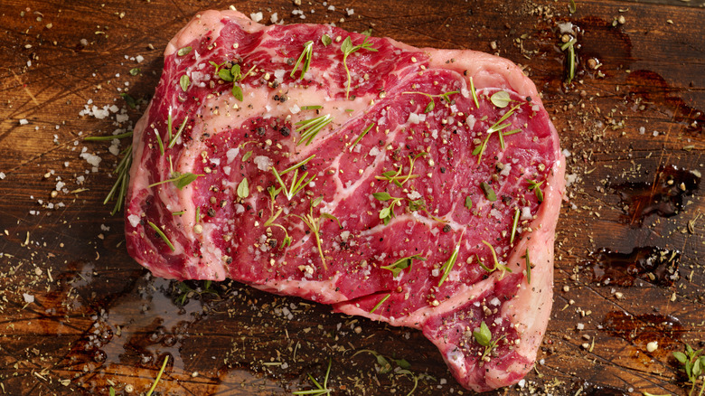 Raw steak seasoned with herbs, salt, and pepper